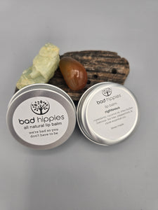 small metal tin filled with all natural lip balm. behind tin is a small piece of driftwood and crystals.